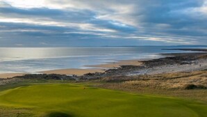 Ein Golfplatz mit Blick auf das Meer und einem bewölkten Himmel.
