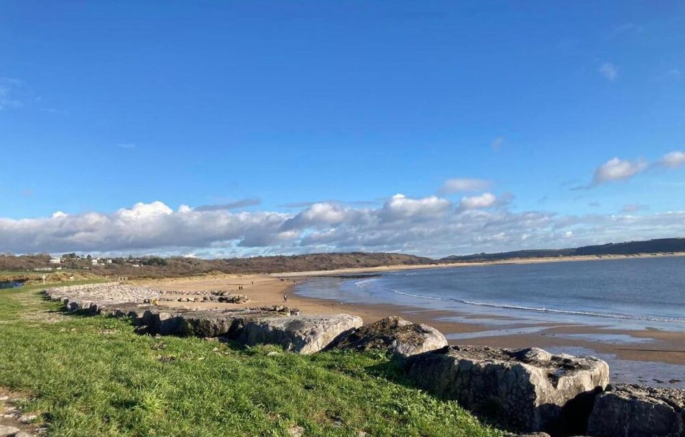 Eine Küstenlandschaft mit blauem Himmel, Sandstrand und Felsformationen.