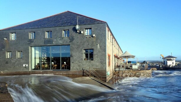 Ein Gebäude mit großem Glas Eingang, einer Fassade aus Stein und Blick aufs Meer.