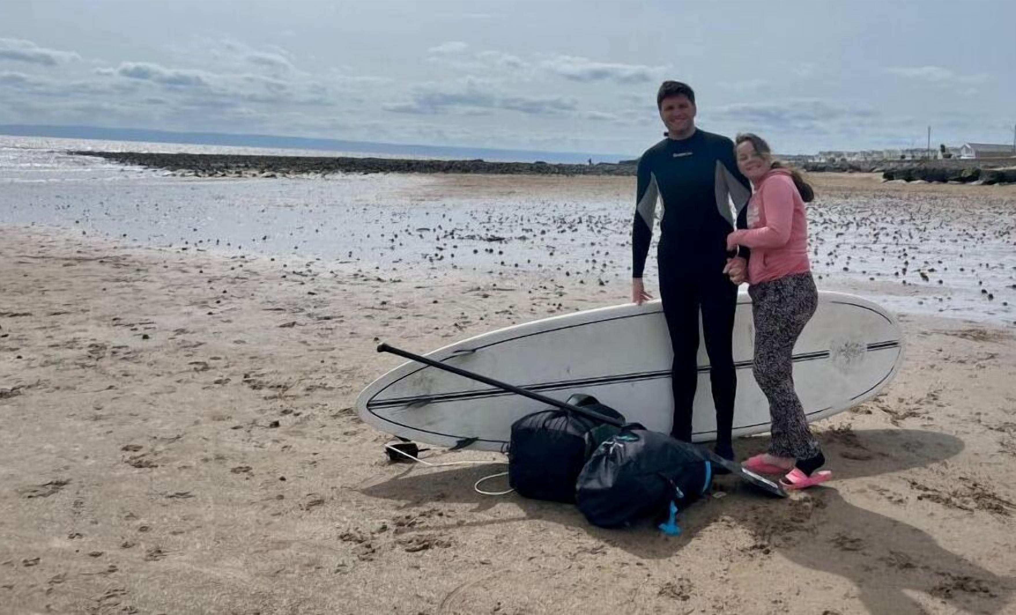 Una playa con una tabla de surf y bolsas en la arena.
