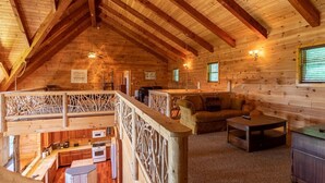 Een houten chalet met slaapkamer op de zolder, een eethoek en een woonkamer met een bank en salontafel.