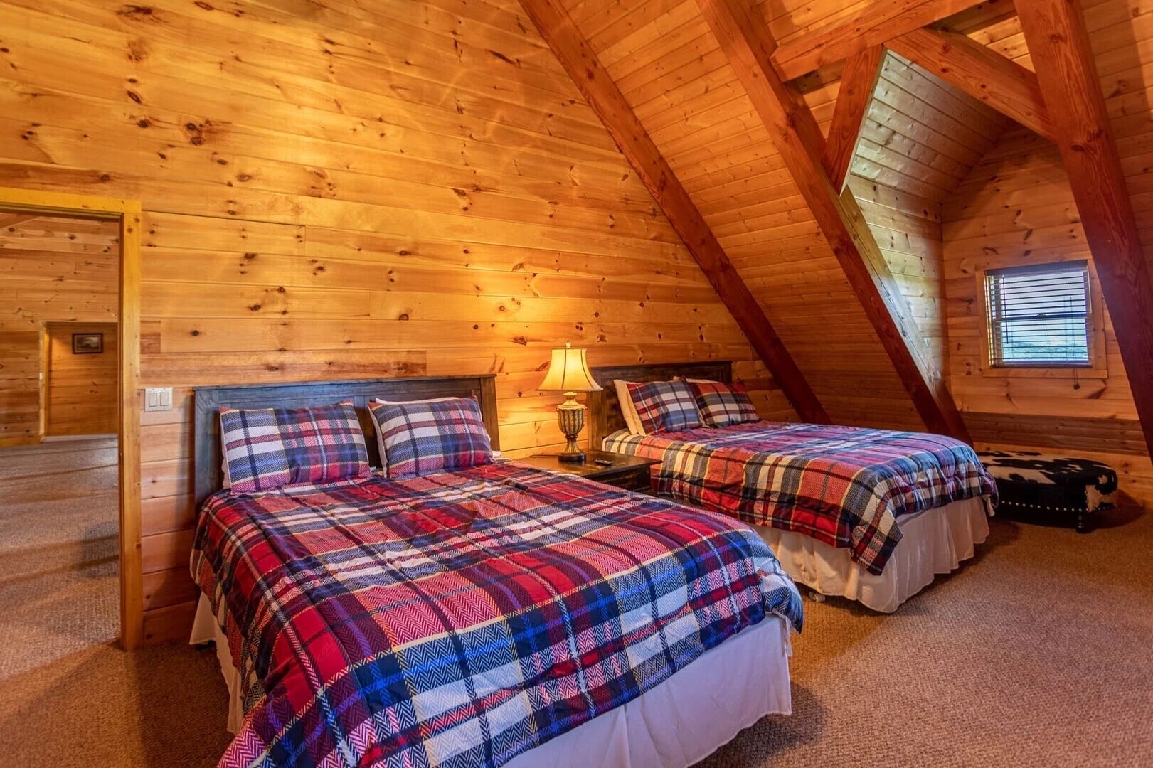 Quarto de sótão aconchegante com duas camas, paredes de madeira e teto inclinado.