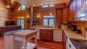 Een ruime keuken met houten kasten, een accentmuur van steen en een groot keukenblok met een spoelbak.
