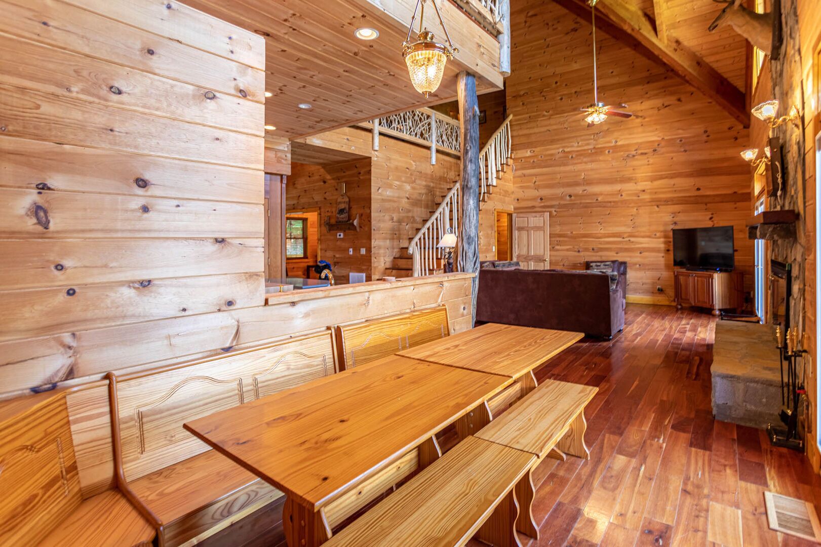 A wooden cabin interior with a dining area, a staircase, a fireplace, and a television.