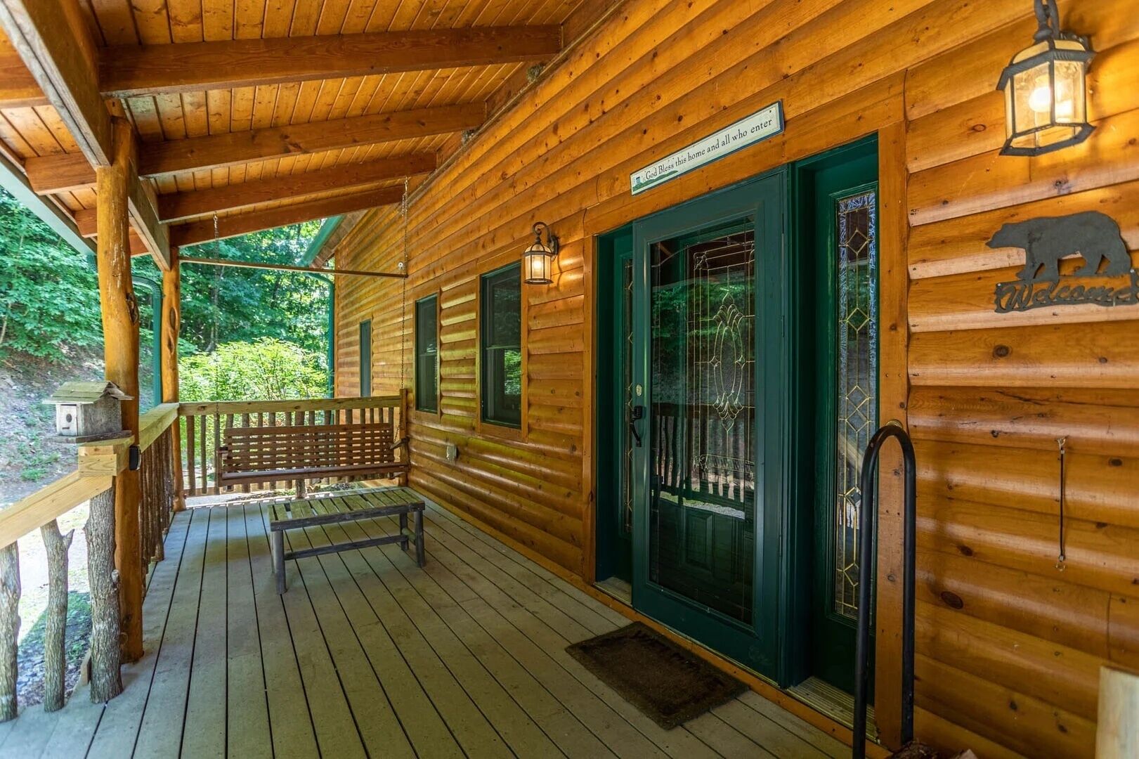 A wooden cabin with a porch, a bench, and a welcome sign.