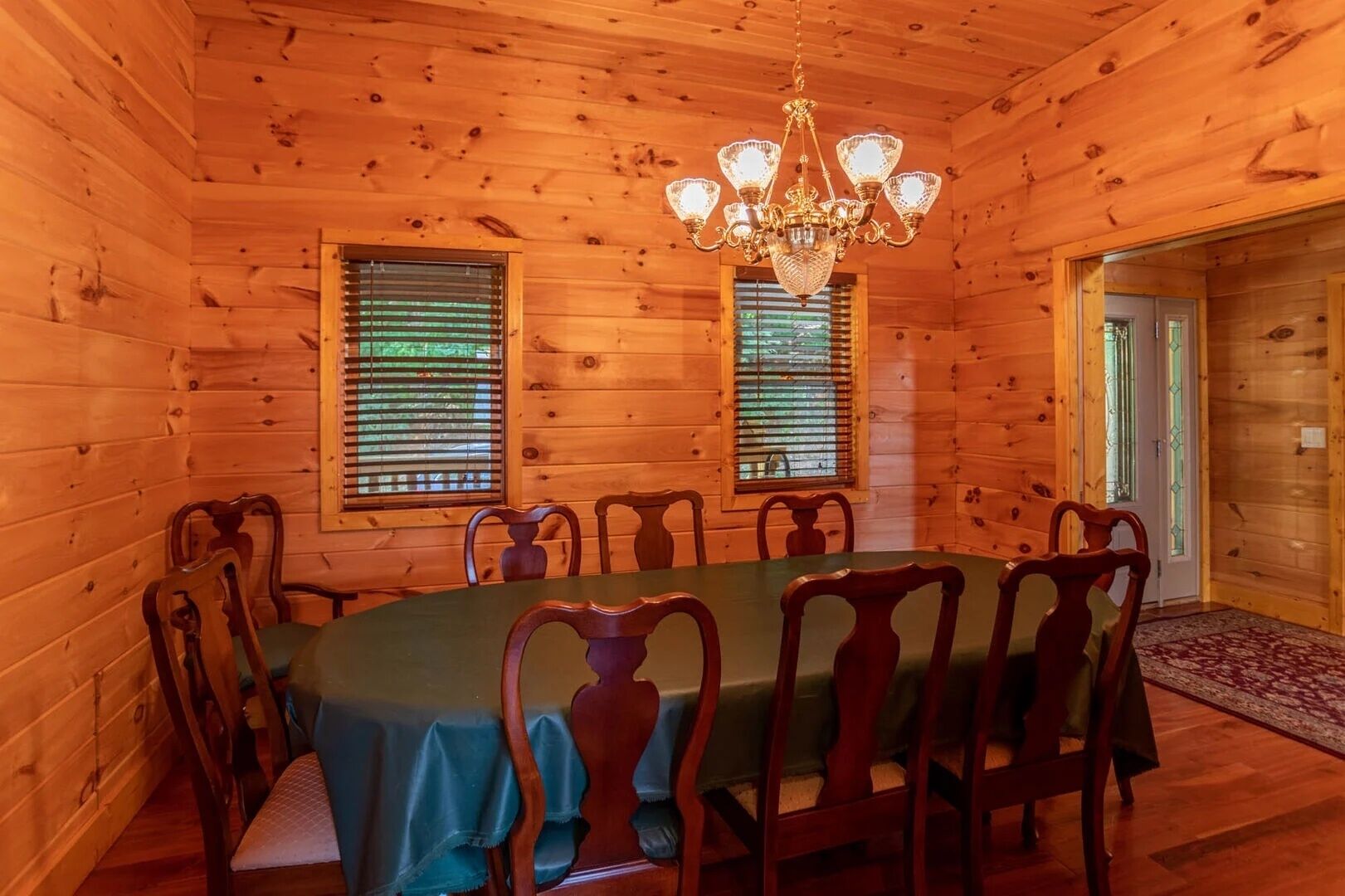 Una sala da pranzo in legno con un tavolo rotondo, sei sedie, un lampadario e due finestre con persiane.