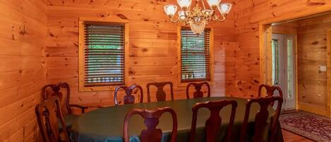 Una sala da pranzo in legno con un tavolo rotondo, sei sedie, un lampadario e due finestre con persiane.