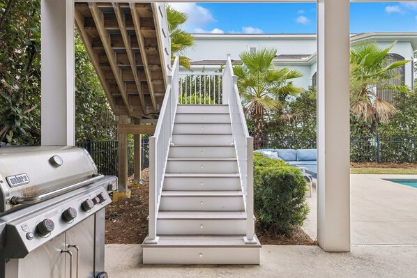 A staircase leading to a covered area with a grill and a pool in the background.