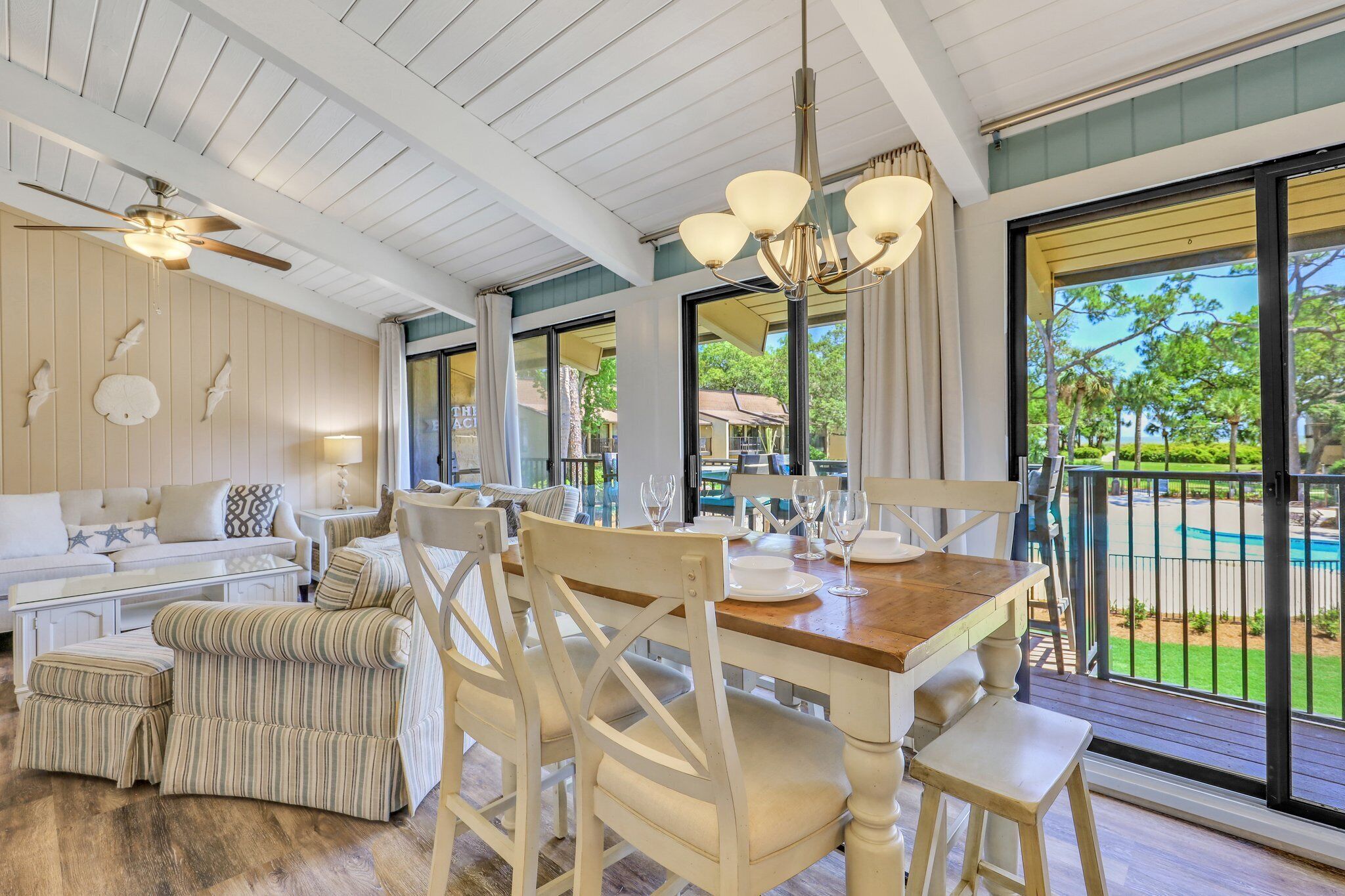 A dining area with a wooden table, white chairs, and a view of a pool.