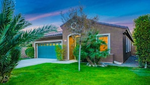A modern two-story house with a garage, surrounded by well-maintained lawns and palm trees. - Flairbnb/Pool/Spa/Pool Table (Indio)