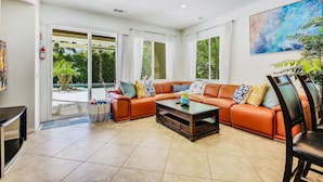 A spacious living room with a large orange sectional sofa, a coffee table, and a ceiling fan. - Flairbnb/Pool/Spa/Pool Table (Indio)