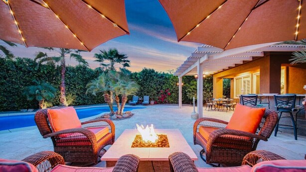 An outdoor patio with wicker furniture, a fire pit, and a pool in the background. - Flairbnb/Pool/Spa/Pool Table (Indio)
