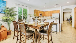 A modern kitchen with wooden cabinets, a central island, and a dining area with a table set for six. - Flairbnb/Pool/Spa/Pool Table (Indio)