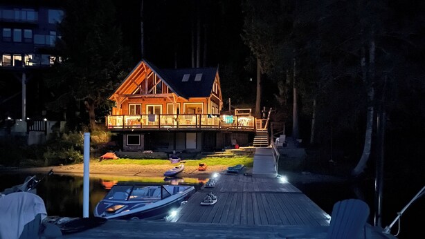 Een houten steiger met boten en stoelen, een huis met terras, en een rustig waterlichaam.
