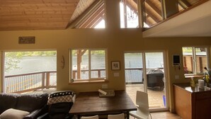 Een chalet met houten inrichting, grote ramen met uitzicht op een meer, een eethoek en een keuken.