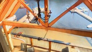 Een houten terras met uitzicht op een meer en boten, een kroonluchter en een balustrade.