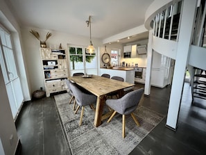 Uma cozinha moderna com armários brancos, uma ilha de madeira e um espaço de refeições com mesa de madeira e cadeiras cinzentas.