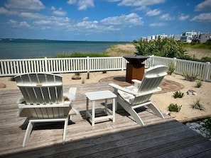 Una terraza con dos sillas Adirondack y una mesita pequeña, con vistas a una playa y al océano.