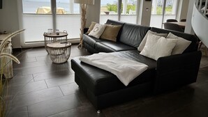 Ein modernes Wohnzimmer mit einer schwarzen Ledersofa, einem runden Couchtisch und Meerblick durch große Fenster.