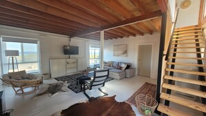 Amplia sala de estar con techo alto, un televisor montado en la pared, un sofá, un sillón y una escalera de madera.