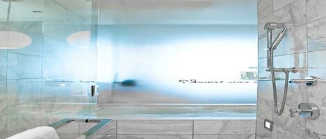 A modern bathroom with a glass shower enclosure, a marble-tiled floor, and a glass bathtub.