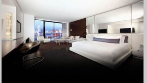 Una habitación de hotel moderna con una cama grande, un área de descanso y vistas a la ciudad, además de un ventanal amplio.