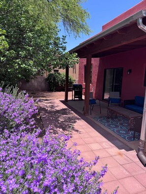 A patio area with a grill, outdoor seating, and purple flowers.