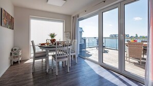A modern dining area with a round table and chairs, a small side table, and a view of a balcony with outdoor seating. - Maisonette Fewo Ostseeflair Erste Wasserreihe, Panoramablick, by Seeblick Ferien (Kappeln)