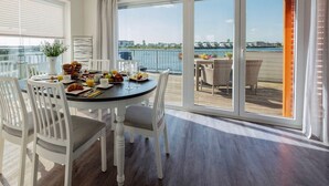 A dining area with a table set for breakfast, overlooking a balcony with a view of the water and buildings. - Maisonette Fewo Ostseeflair Erste Wasserreihe, Panoramablick, by Seeblick Ferien (Kappeln)