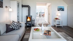 A modern living room with a fireplace, a sofa with patterned cushions, a glass coffee table with fruit and a bottle, and a view to the outside. - Maisonette Fewo Ostseeflair Erste Wasserreihe, Panoramablick, by Seeblick Ferien (Kappeln)