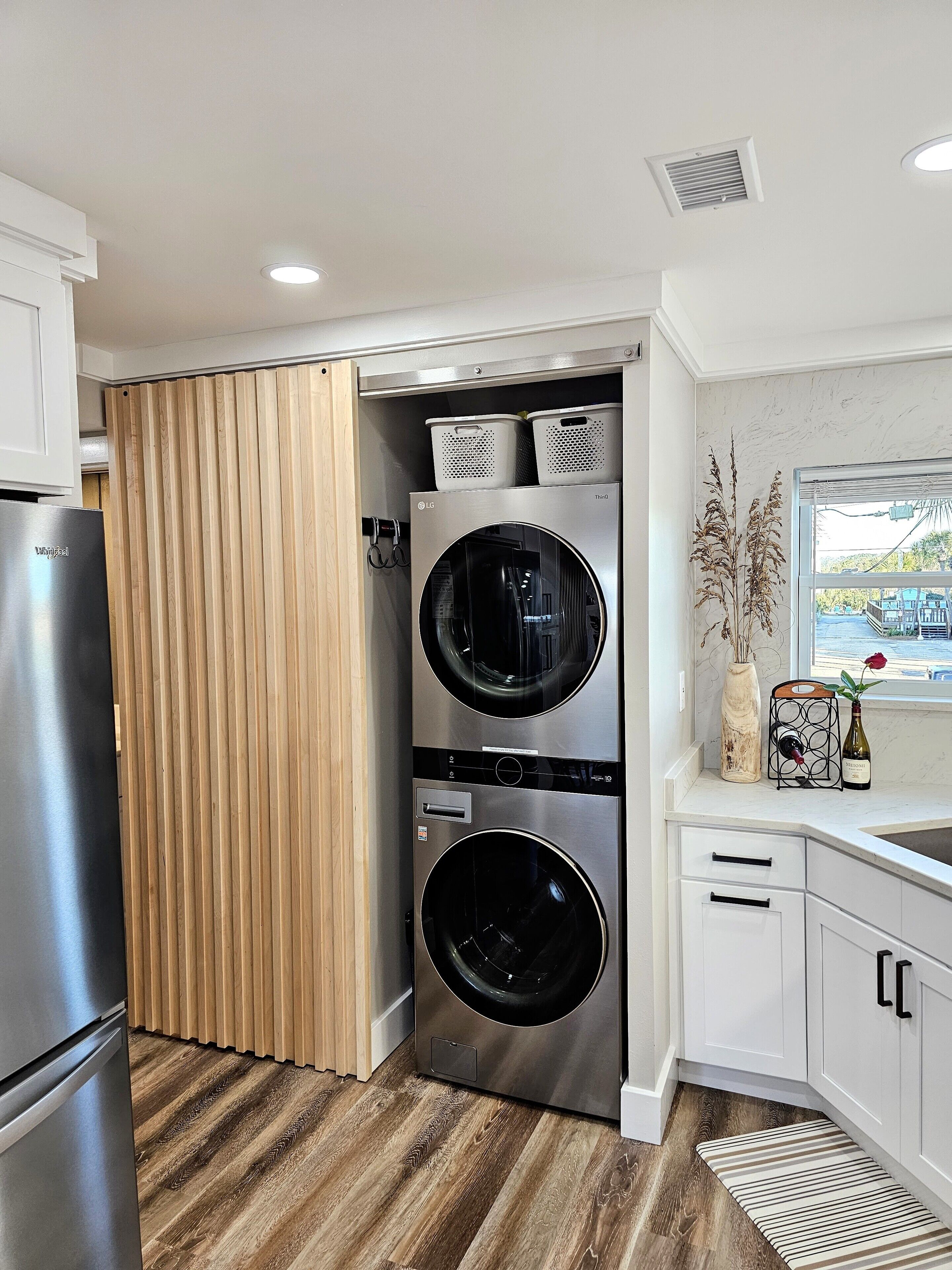 A compact kitchen with a built-in washer and dryer, wooden flooring, and a view of the outside through a window.