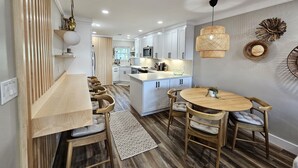 A modern kitchen with white cabinets, a central island, and a dining area with wooden chairs and a round table. - BEACHFRONT Townhome - New Kitchen and Bath - 2 BR 2.5 Bath   (Gulf Shores)