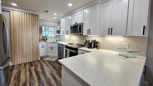 A modern kitchen with white cabinets, stainless steel appliances, and a marble countertop. - BEACHFRONT Townhome - New Kitchen and Bath - 2 BR 2.5 Bath   (Gulf Shores)