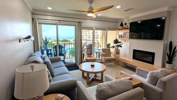 A modern living room with a sofa, armchairs, a coffee table, a TV, and a fireplace. - BEACHFRONT Townhome - New Kitchen and Bath - 2 BR 2.5 Bath   (Gulf Shores)