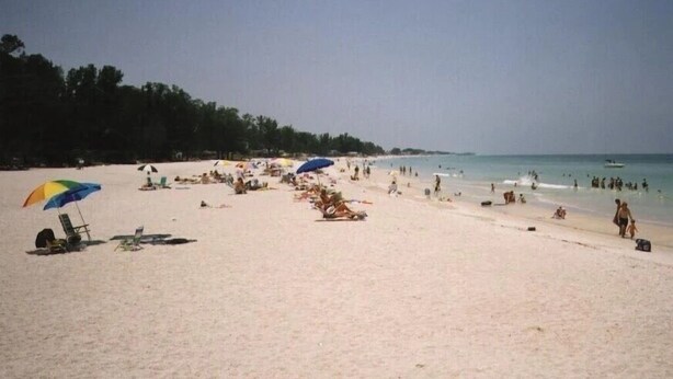 A beach with people sunbathing and swimming, umbrellas, and beach chairs. - Villa-style condo with pool and beach access - Condo 8 (Holmes Beach)