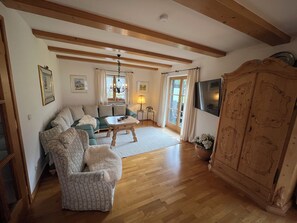 A living room with a sofa, armchair, wooden coffee table, and a television mounted on the wall. - Frühholz—The Vacation Home, 5-Star "Kreuzeck" Apartment in Grainau & Southwestern-Facing Balcony (Grainau)