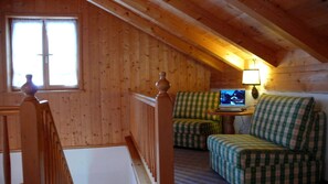 Acogedor dormitorio en el ático con paredes de madera, una ventana, una computadora portátil sobre una mesita y dos sofás a cuadros.