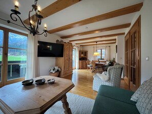 Un salón amplio con una mesa de comedor de madera, un sofá verde y un televisor montado en la pared.
