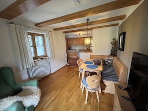 A cozy living area with a sofa, a dining table with chairs, a television, and a kitchen in the background.