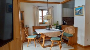 Un comedor con una mesa de madera, cuatro sillas, una lámpara y vistas a una cocina.