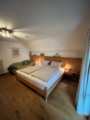 Un dormitorio con una cama de madera, un sofá verde, una mesita de noche con una lámpara y un radiador.