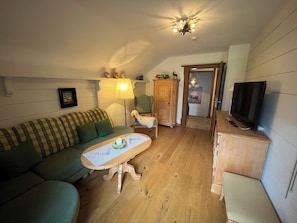 A cozy living room with a green sofa, a wooden coffee table, a television, and a cabinet.