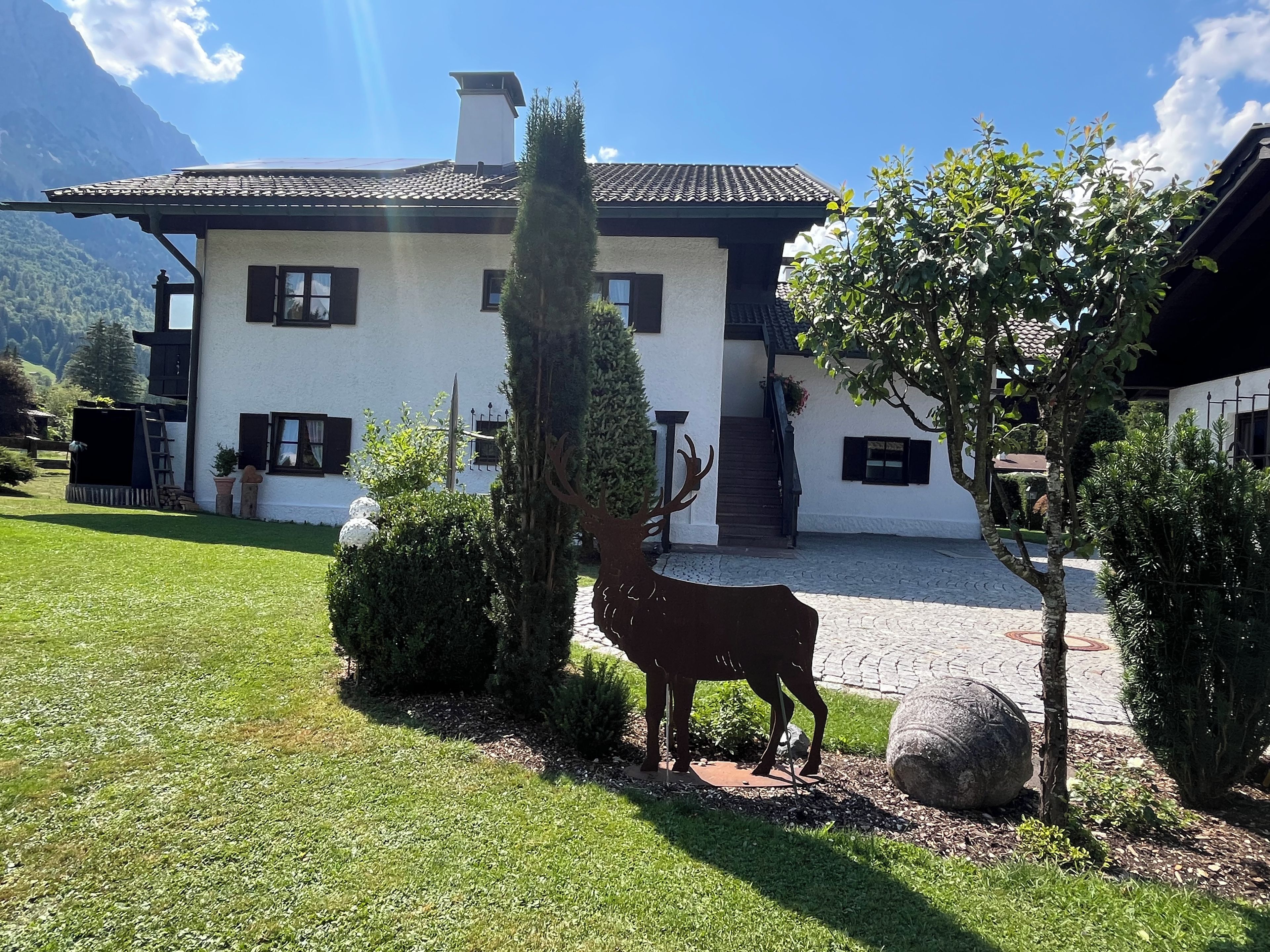 Ein Haus mit einem Ziegeldach, einem Schornstein und einem Vorgarten mit einer Hirschstatue.