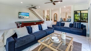 A spacious living room with two dark blue sofas, a wooden coffee table, a pool table, and a staircase leading to another level. - The Palms - Hamilton Island (Hamilton Island)