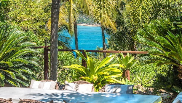 A patio with wicker furniture and a view of a beach. - The Palms - Hamilton Island (Hamilton Island)