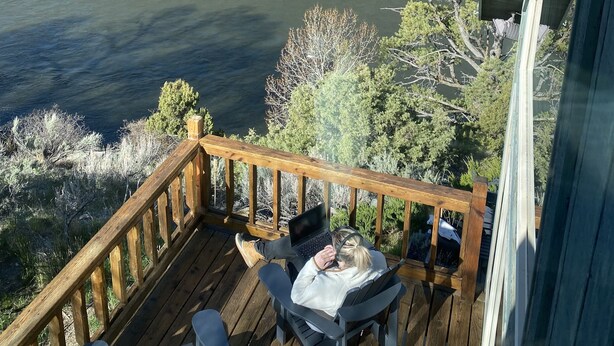 Une terrasse en bois avec une table et des chaises, donnant sur une rivière et des collines.