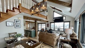 Un vaste espace de vie agrémenté d’un escalier en bois, d’une table à manger avec un set de table en peau de vache, d’un canapé et d’une lampe.