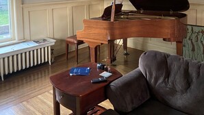 A grand piano in a room with a radiator, a framed landscape painting, and a sofa. - Classic uptown mansion (Butte)