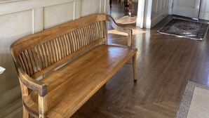 A wooden bench in a hallway with a framed painting on the wall, a piano, and a door labeled 1039. - Classic uptown mansion (Butte)