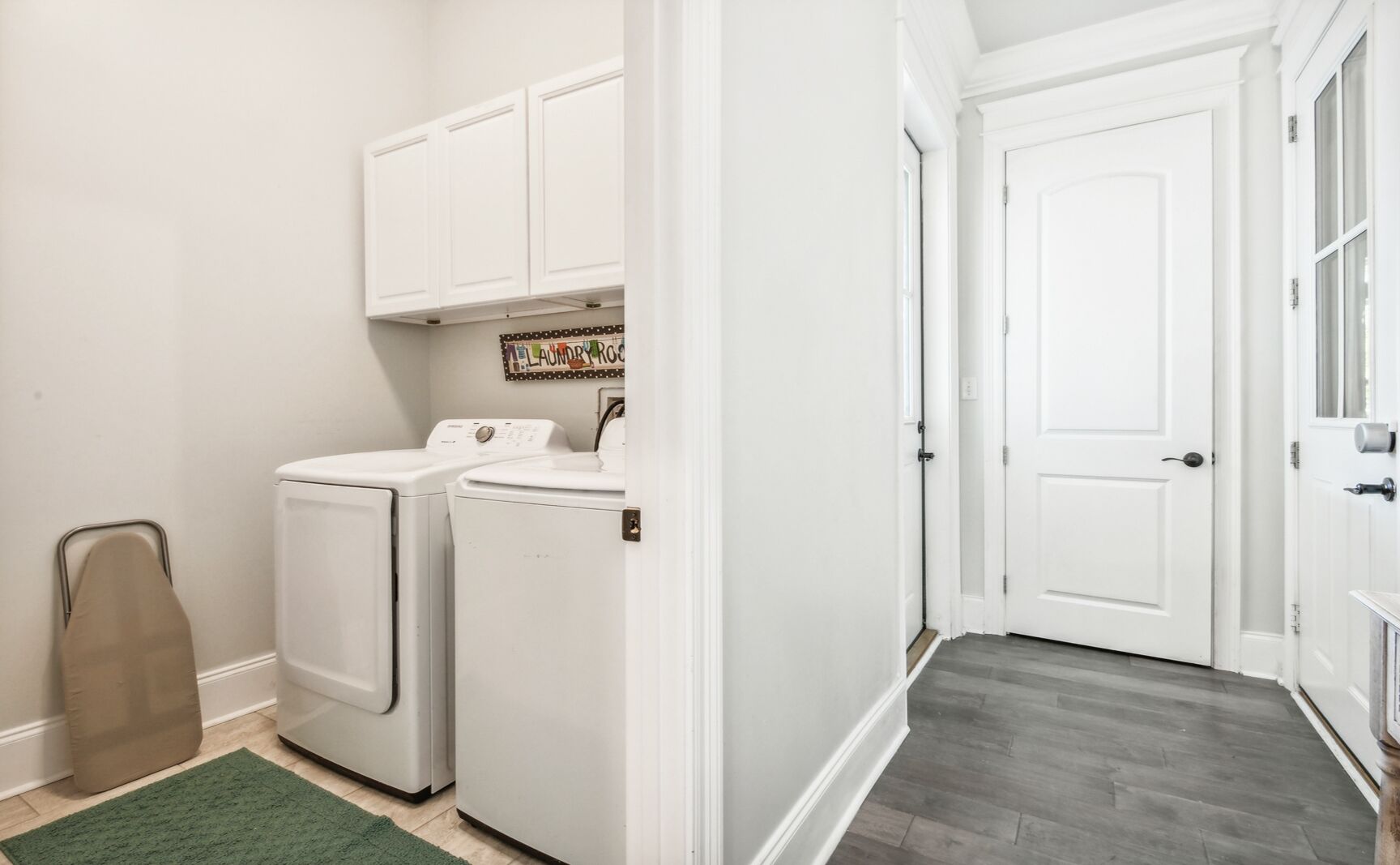A laundry room with two white washing machines, a drying rack, and a door leading to another room.